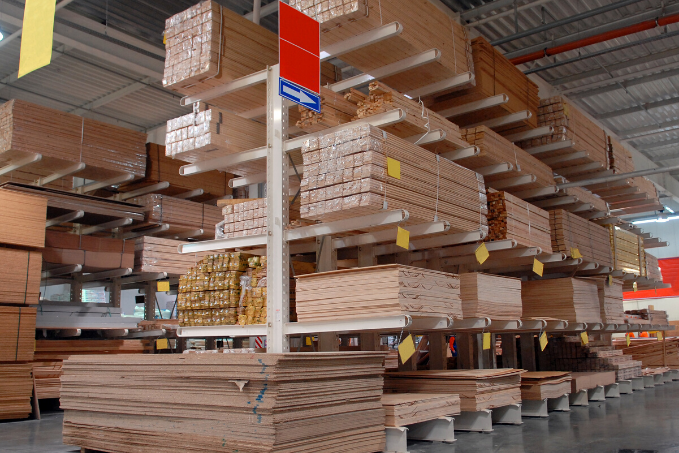 A warehouse with tall shelving units filled with neatly stacked wood and wood products, labeled with color-coded signs for organization.