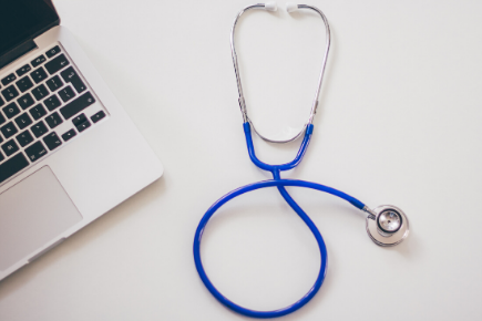 An open laptop beside a coiled blue stethoscope on a white surface.