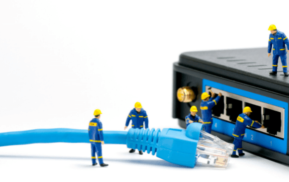 Miniature figures dressed as technicians working on a large Ethernet cable and network switch, with one figure holding a small golden globe, against a white background.