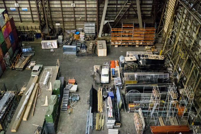 Aerial view of an industrial warehouse with organized sections of construction materials, metal beams, racks, and equipment.