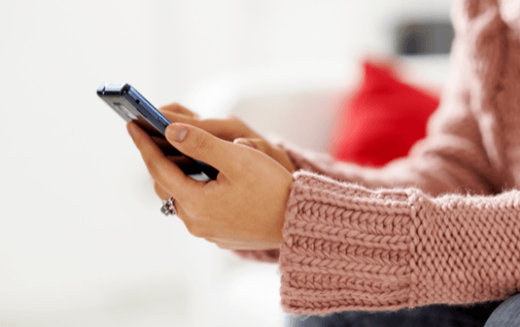 Close-up of hands holding a smartphone with a pink sweater sleeve and a red cushion in the background.