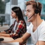 A young man and a woman wearing headsets and working at computers in an office setting, possibly as customer service representatives.