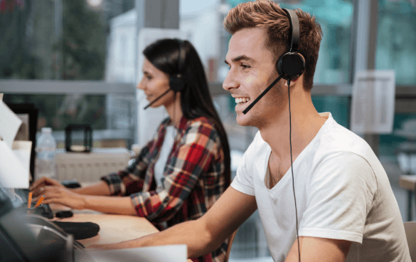 A young man and a woman wearing headsets and working at computers in an office setting, possibly as customer service representatives.