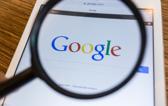 A magnifying glass is held over a tablet screen displaying the Google homepage.