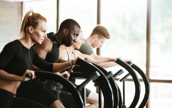 Four people working out on elliptical machines in a bright gym.