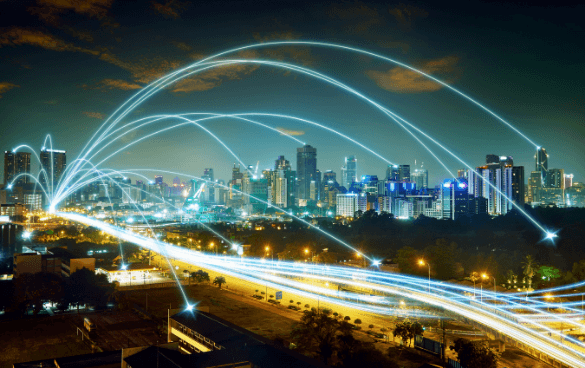 Nighttime cityscape with illuminated buildings and a busy highway, overlaid with curved light trails symbolizing connectivity or digital networks.