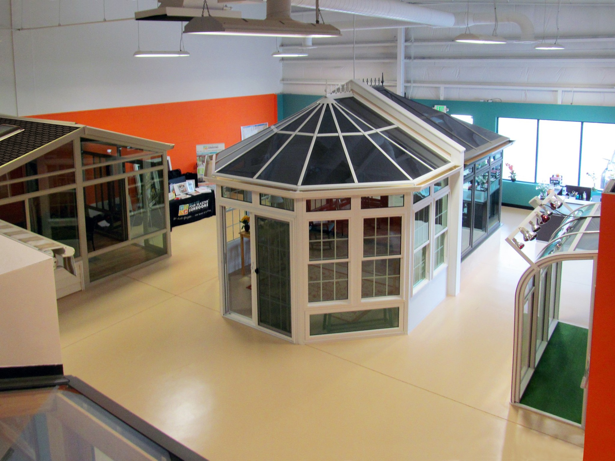 Indoor showroom with models of conservatories and sunrooms in different designs and roofing styles, brightly lit with a two-tone painted wall in the background.