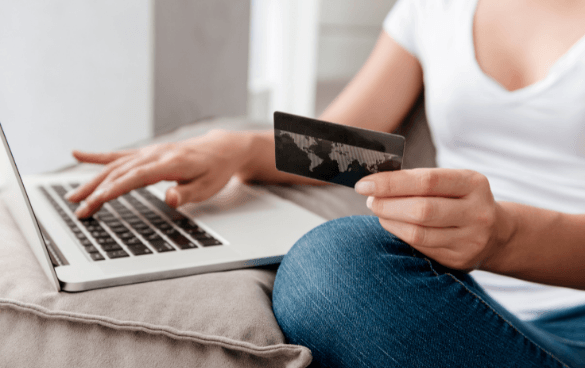 A person sitting with a laptop on their lap, holding a credit card in one hand and typing with the other.