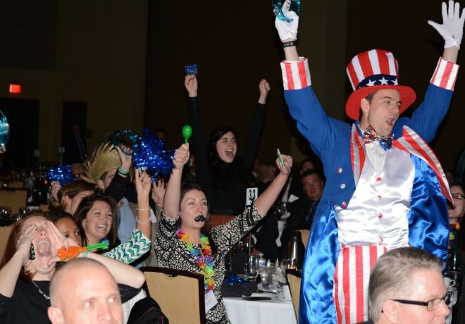 A man dressed as Uncle Sam with raised arms is surrounded by cheering people at a festive event.