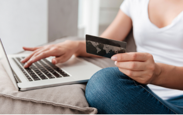 Person sitting on a couch using a laptop and holding a credit card, possibly engaging in an online transaction.