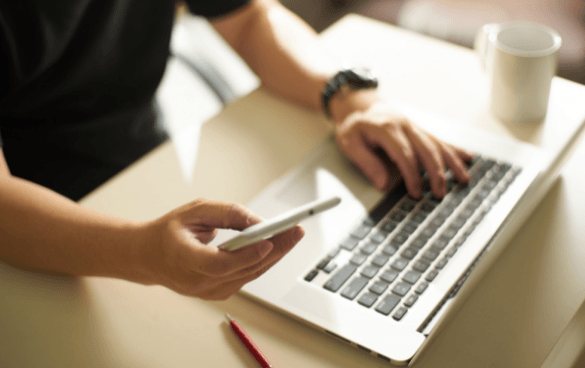 Person using a cell phone while browsing on a computer