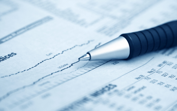 A ballpoint pen resting on a financial newspaper with stock market graphs and data, indicating analysis of financial information.