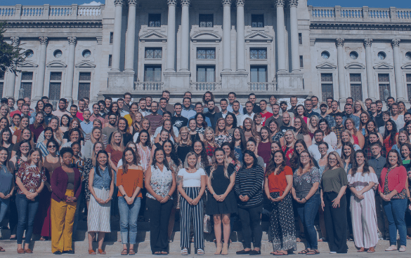 A diverse group of people standing on the steps of a grand building with classical architecture, possibly a government or institutional building.