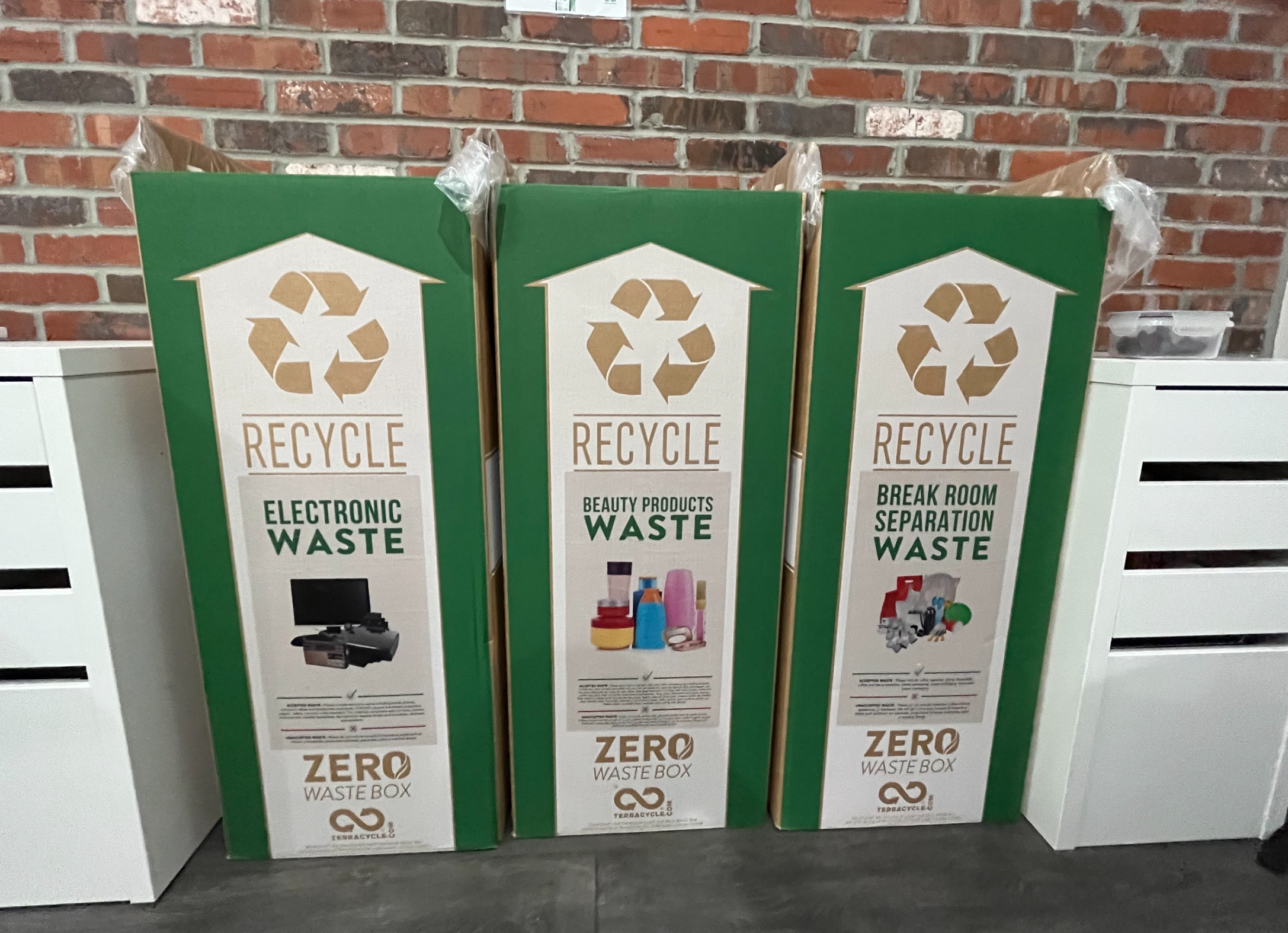 Three recycling bins labeled for electronic waste, beauty products waste, and break room separation waste, with corresponding images of the waste types and TerraCycle's Zero Waste Box logo.