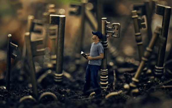 A miniature figure reading a book in a whimsical forest of oversized keys planted in the ground.