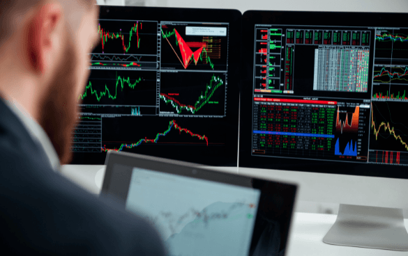 A person analyzing financial charts on multiple computer monitors in a professional setting.