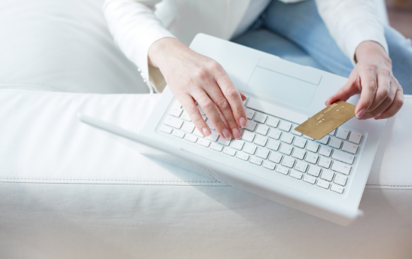 Person using a white laptop and holding a credit card, possibly making an online purchase.