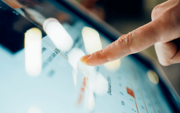 Close-up of a finger touching a tablet screen displaying charts and data.