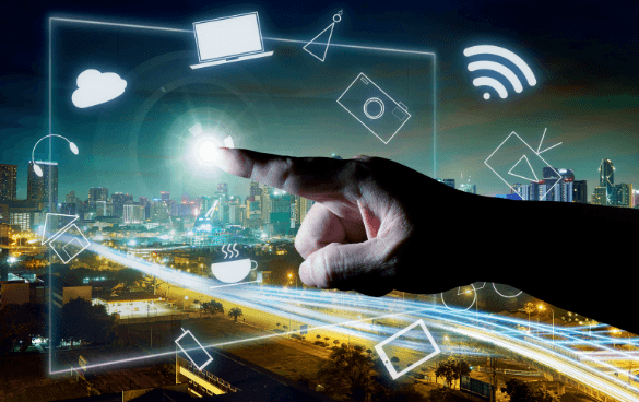 A human hand interacting with floating digital icons representing cloud computing, Wi-Fi, and multimedia over a night cityscape background.