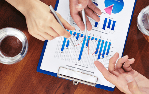 Two people discussing data shown on a clipboard with bar and pie charts, with glasses of water on the table, indicating a business analysis or meeting.