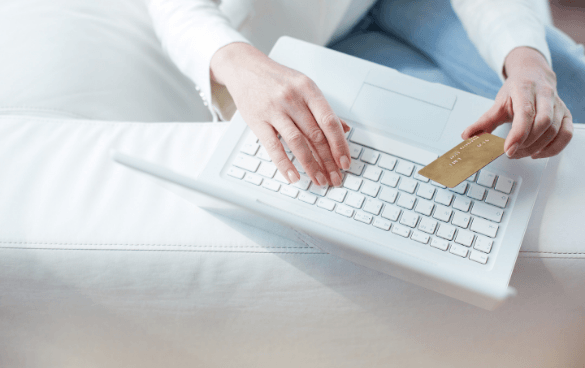 Person using a white laptop and holding a credit card, possibly engaging in an online transaction.