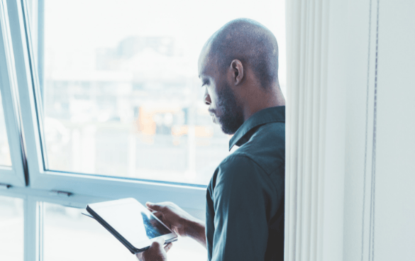 Man standing by a window scrolling on his tablet