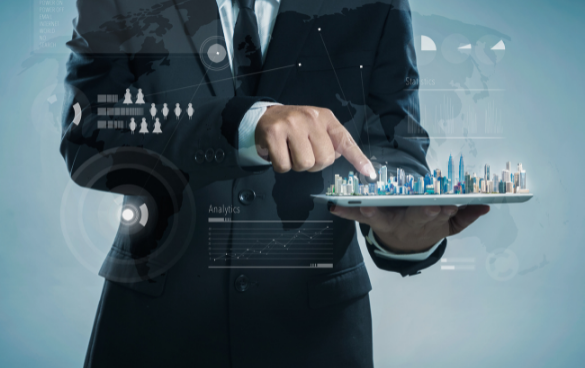 A person in a business suit holding a tablet that projects a holographic cityscape, pointing at one of the skyscrapers, with digital graphs and interface elements around it.