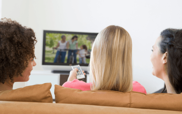 Two women sitting on a couch watching television, with one holding a remote control.