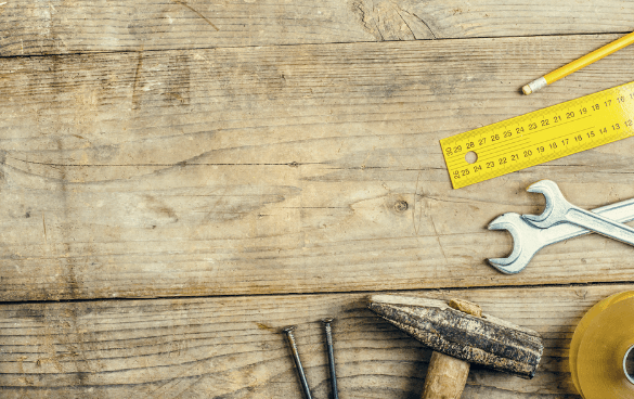 Carpentry tools including a measuring tape, hammer, wrench, pencil, and nails on a wooden surface.