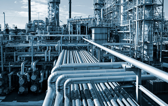 Monochromatic blue-tinted image of a complex industrial facility with an intricate network of pipes and structures, indicative of a chemical plant or refinery.