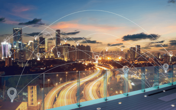 Twilight cityscape with illuminated buildings and a busy highway, overlaid with a graphic representation of a smart city network with lines and nodes.