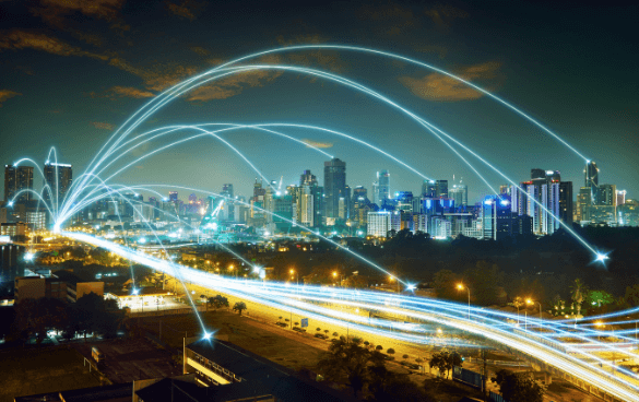 Nighttime cityscape with illuminated buildings and a highway, overlaid with curved light trails representing connectivity or data transfer.