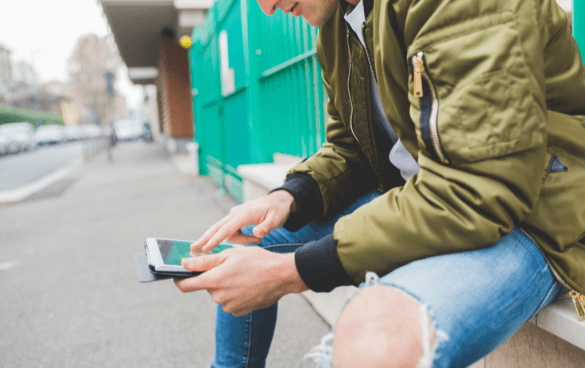 Man sitting on a ledge scrolling through his phone