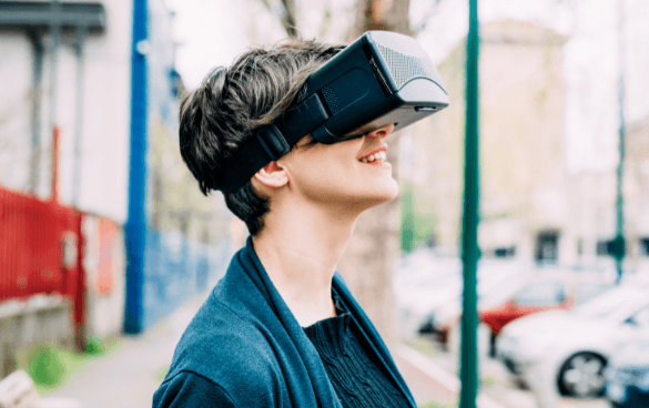 Person smiling while wearing a virtual reality headset outdoors with blurred urban background.