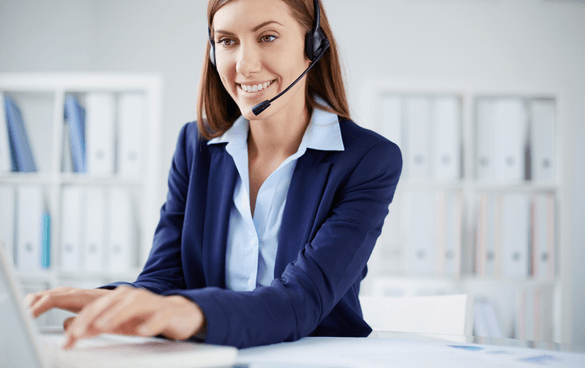 A smiling woman with a headset working on a laptop in an office setting.