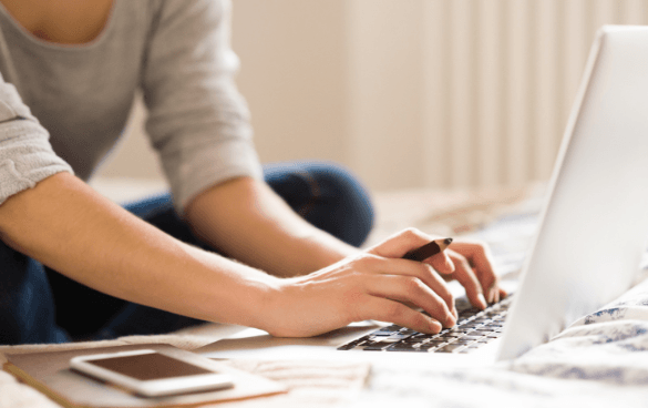 Woman typing on a computer while holding a pen