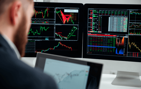 A person analyzing financial charts and data on multiple computer monitors in a trading or analysis environment.