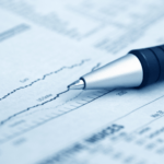A pen resting on a financial newspaper displaying stock market graphs and data.
