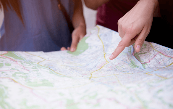 Two people looking at a paper map with one person pointing at a location on the map.