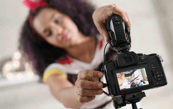 A young girl with curly hair adjusts a DSLR camera mounted on a tripod, focusing on the camera's screen and controls.