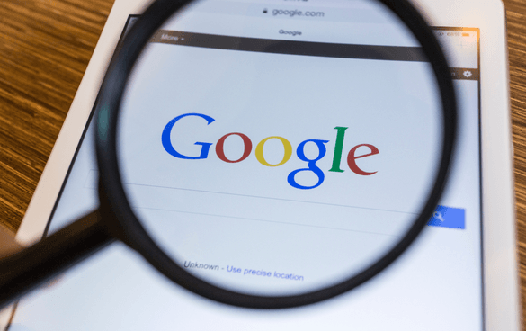 Magnifying glass enlarging the Google logo on a tablet screen with a wooden surface background.