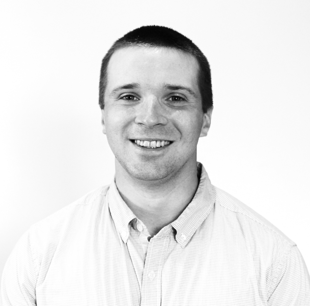 Black and white portrait of a smiling man wearing a button-up shirt.