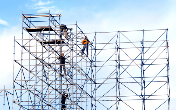 Workers on a multi-level metal scaffolding structure with safety gear against a blue sky with clouds.