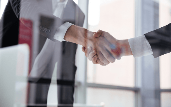 Two individuals in business attire shaking hands in an office environment.