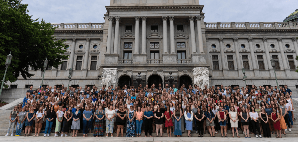 A large group of people posing for a group photograph on the steps of a grand building with classical architecture.