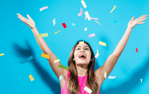 Joyful woman with raised arms celebrating with colorful confetti against a blue background.