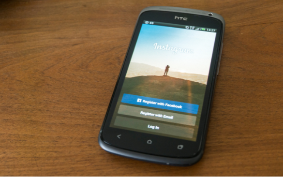 HTC smartphone on a wooden surface displaying the Instagram login page with registration and login options.