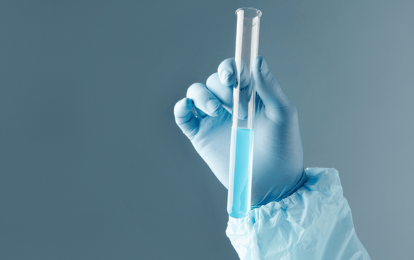 Person in a blue glove holding a test tube with blue liquid against a neutral background.