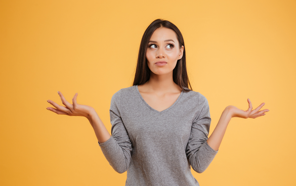 Puzzled young woman with raised hands, looking to the side, against a yellow background.