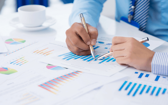 Two people analyzing and discussing colorful charts and graphs on paper with a coffee cup on the table.